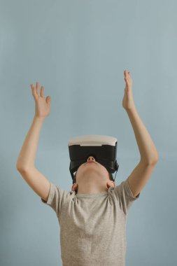 Sanal gerçeklik gözlüklü çocuk. Eller yukarı. Mavi arka plan