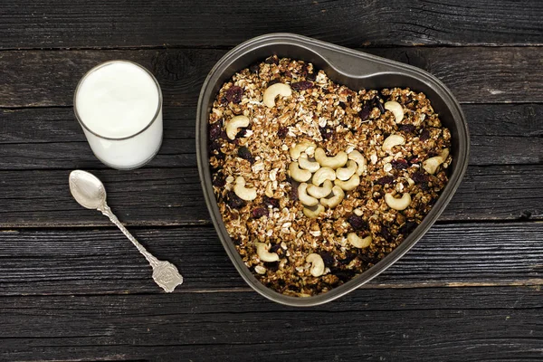 Bardak yoğurt ve bir fırın tepsisine kaju granola. Siyah ahşap masa