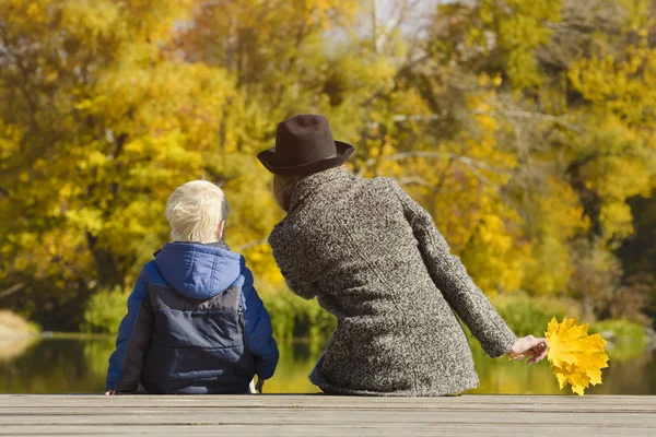 Sarışın çocuk ve annesi iskelede oturuyordu. Sonbahar günü. Arkadan görünüm
