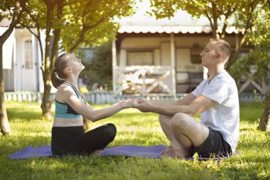 İki aşık yoga yapmak için halıya oturup el ele tutuşurlar. Yaz bahçesinde sabah
