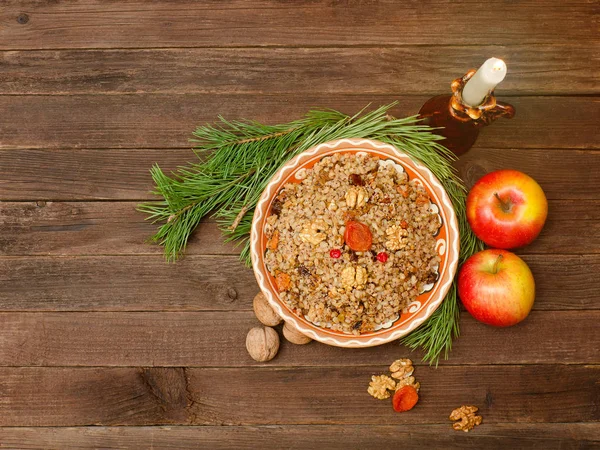 Dish of traditional Slavic treat on Christmas Eve.  Pine branche, apples, walnuts and candle. Brown wooden background. Top view. Copy space