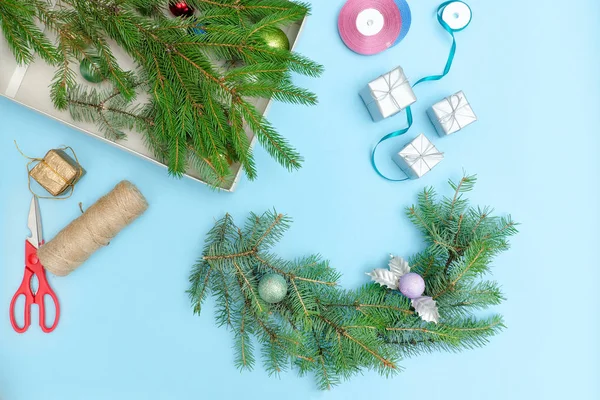 Making a Christmas wreath. Spruce branch, ornaments, scissors. Blue background.