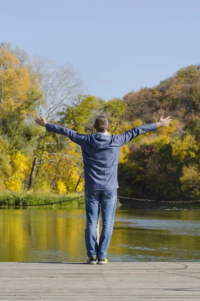 Man with arms raised standing on the dock. Autumn, sunny. Back view