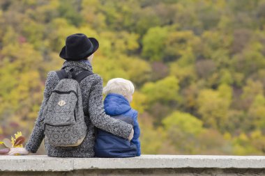 Anne ve oğlu bir yüksek yerde oturuyorsun. Sonbahar. Mesafe ormanda. Arkadan Görünüm