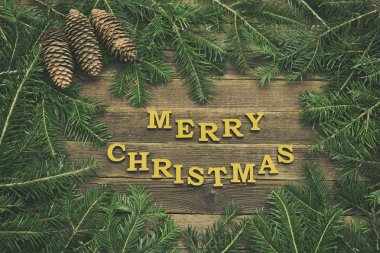 Ahşap arka plan üzerinde yazıt neşeli Noel. Çerçeve çam dalları ve koniler yapılmış. Tatil kavramı