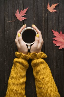 Bir fincan kahve bir kadın elinde. Ahşap arka plan, sonbahar yaprakları. Üstten görünüm