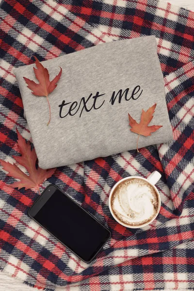 Gray sweater, plaid, coffee mug and smart phone. Autumn leaves. Fashionable concept