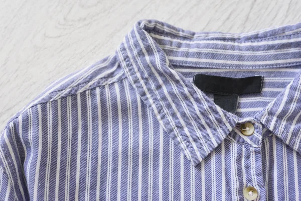 Collar of a blue striped shirt on wooden background. Fashionable concept