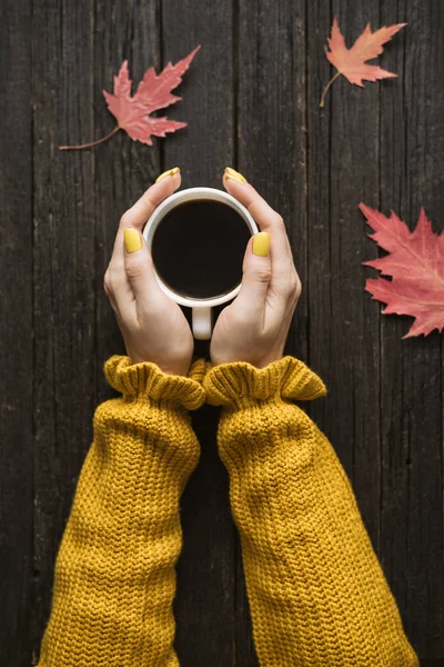 Bir fincan kahve bir kadın elinde. Ahşap arka plan, sonbahar yaprakları. Üstten görünüm