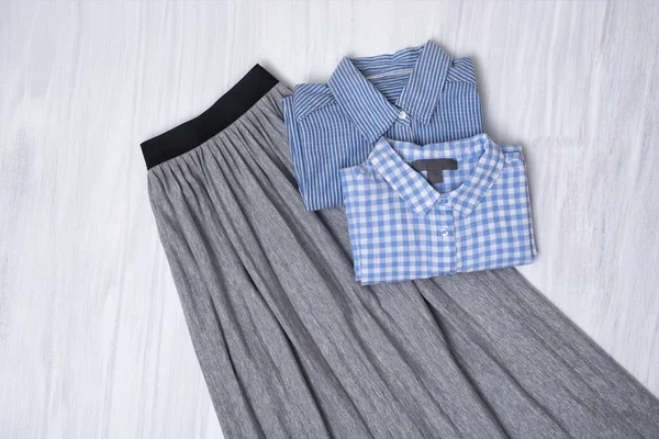 Gray pleated skirt and blue shirts on wooden background. Fashionable concept