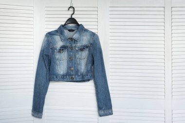 Denim ceket bir askı. Beyaz ahşap arka plan. Şık gardırop