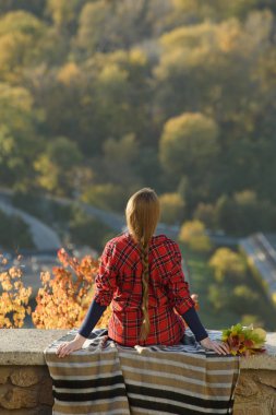 Genç kadın şehir manzaralı bir tepenin üzerinde oturur. Arkadan görünüm