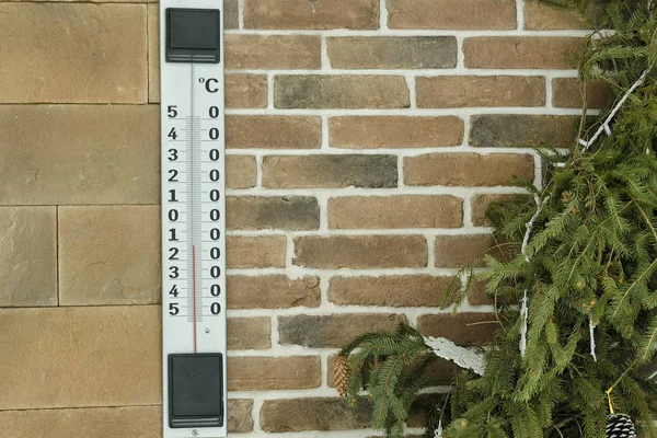 Large outdoor thermometer on a brick wall. Spruce branch.