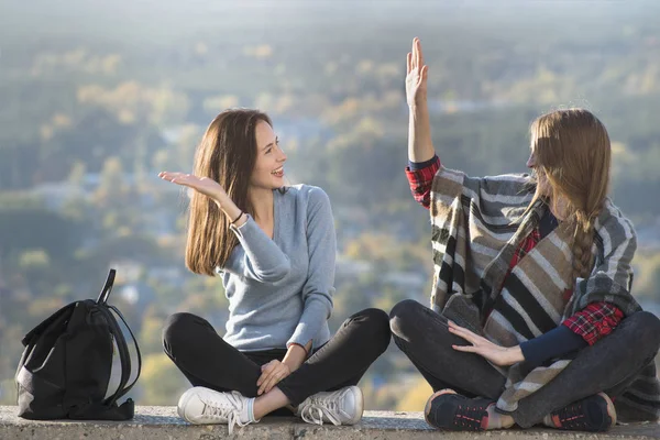 İki gülümseyen kadın çak bir tepe üzerinde oturuyor. Güneşli gün