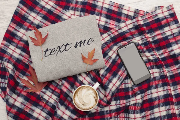 Gray sweater, plaid, cup of coffee and smart phone. Autumn leaves. Fashionable concept