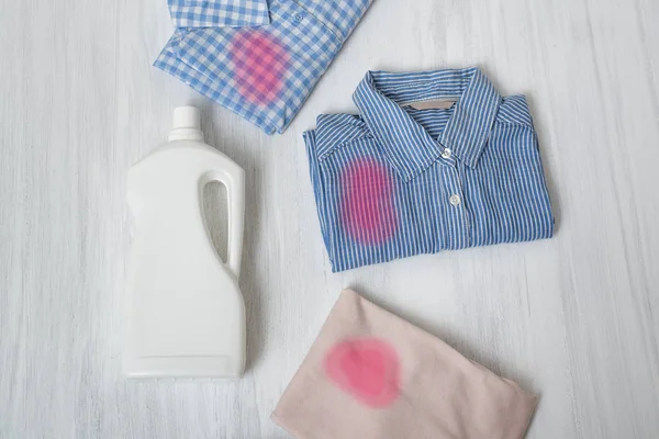 Clothes with stains and a bottle of detergent. Top view