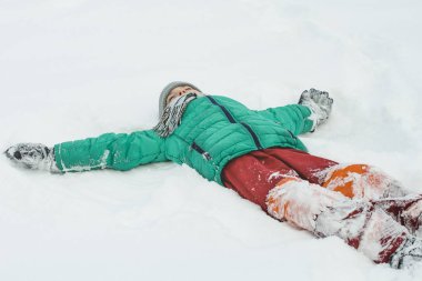 Yeşil bir ceket ve kırmızı pantolon kar sırtına uzanmış silahlarla yatan çocuk. Kış günü