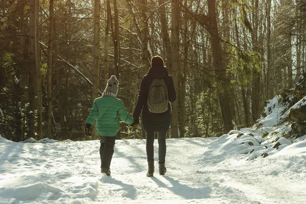 母亲带着儿子走在针叶林的背景下 沿着被雪覆盖的道路走着 冬季晴天 — 图库照片
