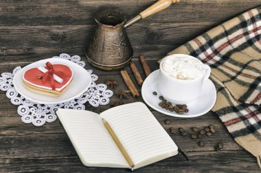 Fincan kapuçino, kalp kurabiye genişliği kahverengi ahşap bir masa üzerinde mesaj, defter, kalem ve kahve kap şeklinde. Tatil planlama