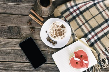 Fincan kapuçino, kalp kurabiye genişliği kahverengi ahşap bir masa üzerinde mesaj, smartphone ve kahve kap şeklinde. Tatil planlama