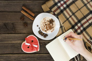 Bayram sabah planlama. Fincan kapuçino, el ile bir kalem ve bir kahverengi ahşap masa üstünde not etmek.