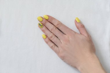 Beyaz kumaş üzerine sarı manikür ile el. Yakın çekim.