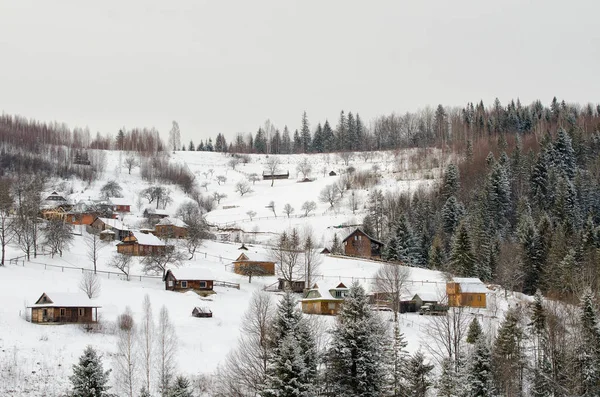 Snow-covered hills, forest and houses in the distance. Winter landscape