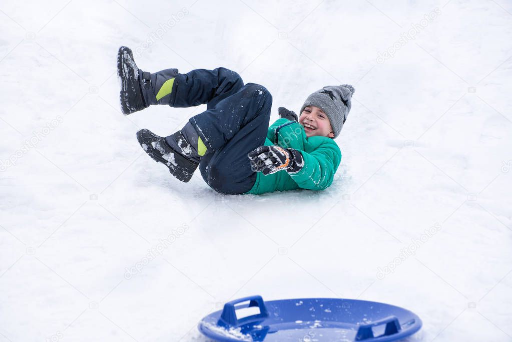 Boy falls rolling down a hill on snow saucer. Winter games.