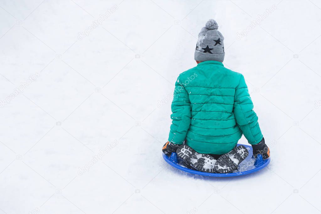 Boy slides down the hill back on snow saucer. Seasonal concept. Winter day.