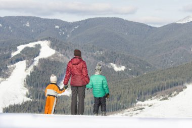 Anne ve iki oğlu karla kaplı dağlar bir arka plan üzerinde duruyor. Arkadan görünüm. Kış güneşli gün
