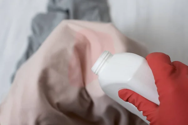 Gloved hand pouring the washing liquid onto the stain on clothes. Close up