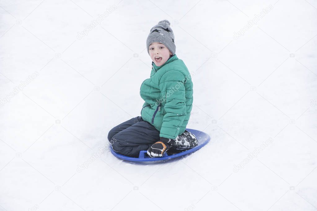 Frightened boy slides down the hill on snow saucer. Seasonal concept. Winter day.