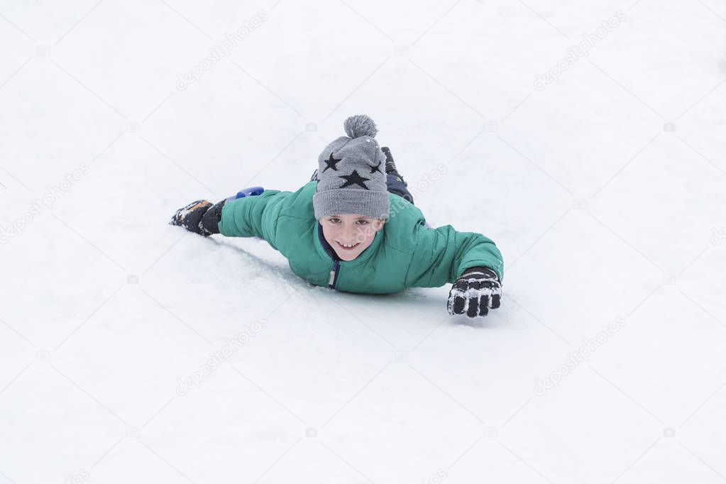 Laughing boy rides on his stomach from a hill. Seasonal concept. Winter day.