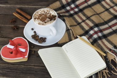 Fincan kapuçino, kalp şekilli kurabiye genişliği mesaj, defter ve kahverengi ahşap bir masa üzerinde kareli ekose. Tatil planlama