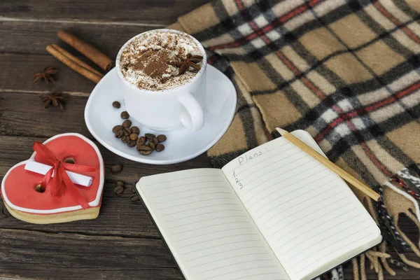 Fincan kapuçino, kalp şekilli kurabiye genişliği mesaj, defter ve kahverengi ahşap bir masa üzerinde kareli ekose. Tatil planlama