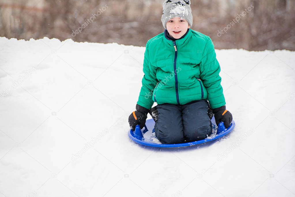 Happy boy slides down the hill on snow saucer. Seasonal concept. Winter day.