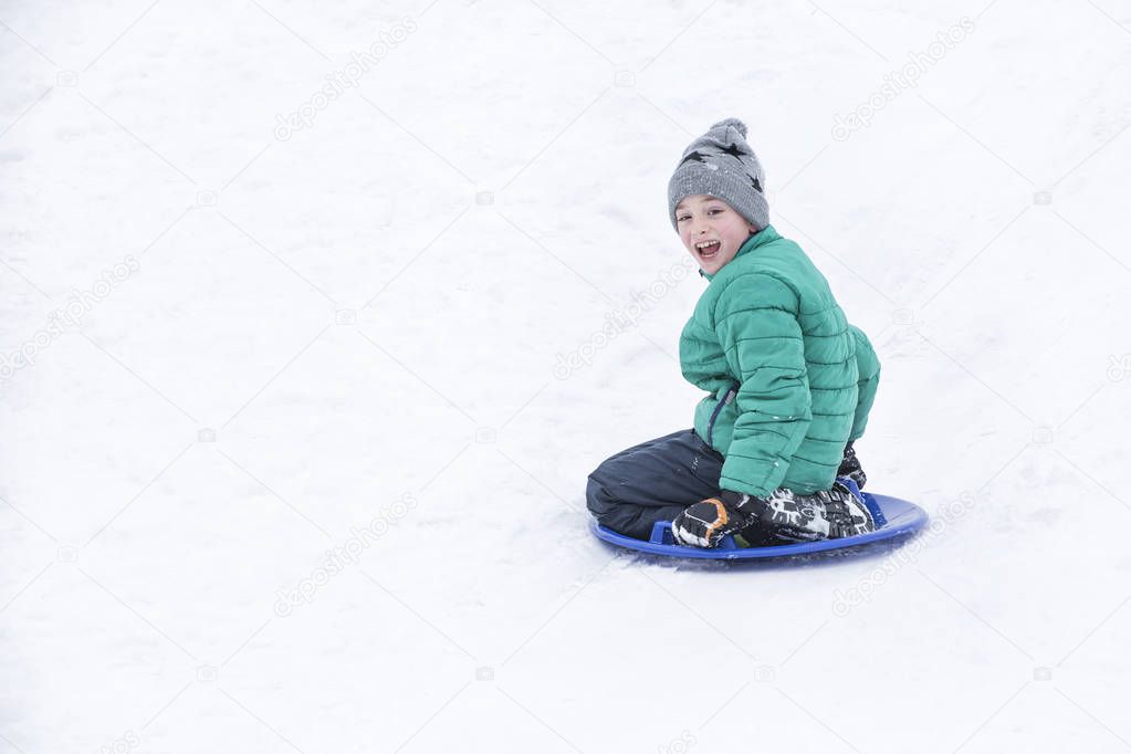 Happy laughing boy slides down the hill on snow saucer. Seasonal concept. Winter day.