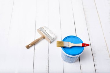 House renovation concept. Two paintbrushe and paint bucket on a background of white, shabby wooden planks.