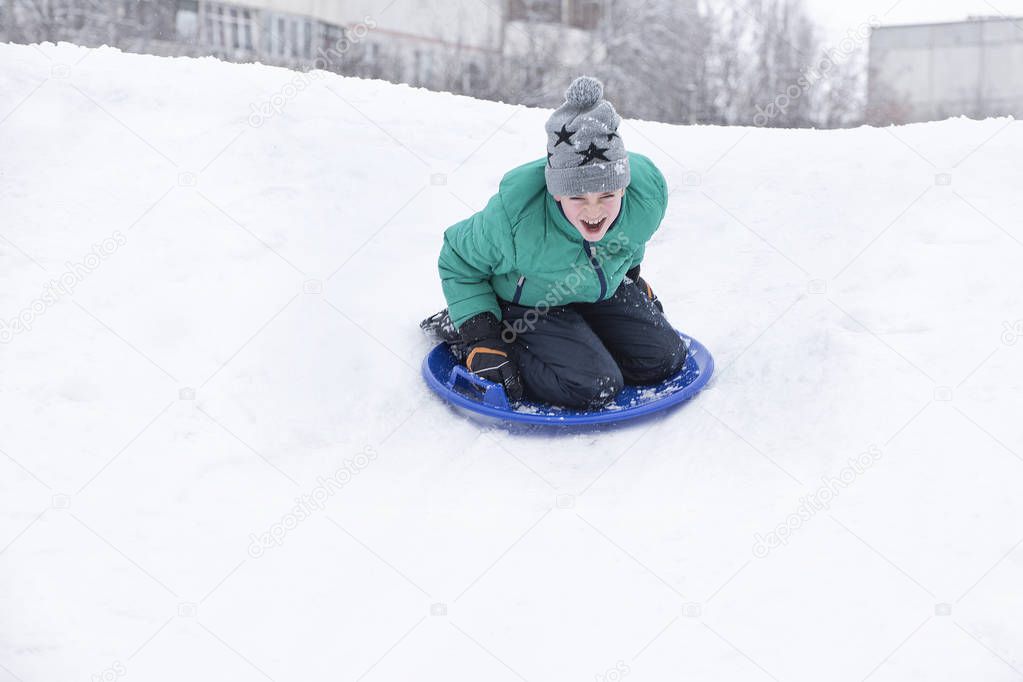 Screaming boy slides down the hill on snow saucer. Seasonal concept. Winter day.