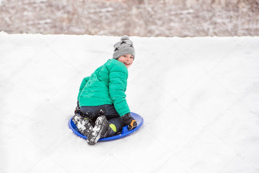 Happy laughing boy slides down the hill on snow saucer. Seasonal concept. Winter day.