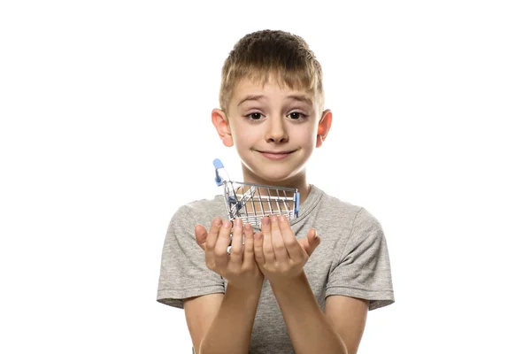 かわいい笑顔の少年は 手に小さな金属のショッピングトロリーを保持しています 白い背景に分離します ショッピングコンセプト — ストック写真