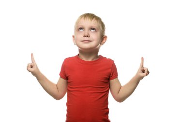 Küçük sarışın çocuk T-shirt duran ve yukarı doğru dizin parmaklarıyla işaret eden bir kırmızı gülümseyerek. Beyaz arka plan üzerinde izole