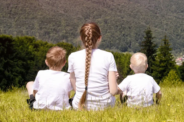 Anne ve iğne yapraklı orman ve dağlar arka plan çimlerde oturan iki genç oğlu.