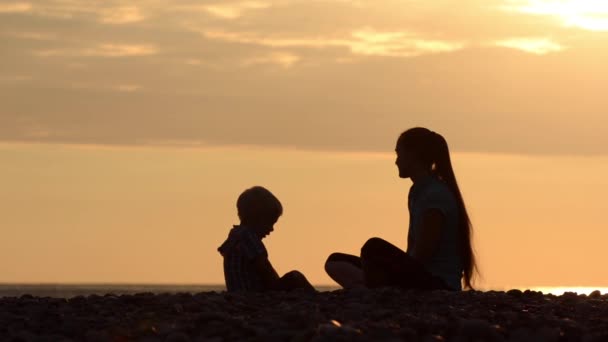 妈妈和儿子在海滩上 石头玩 日落的时候剪影 — 图库视频影像
