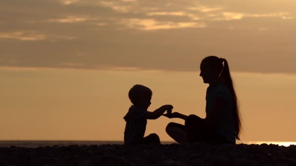 妈妈和儿子在海滩上 石头玩 日落的时候剪影 — 图库视频影像