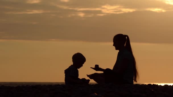 Anne Küçük Oğlu Taşlarla Sahilde Oynarken Günbatımı Zamanı Siluetleri — Stok video