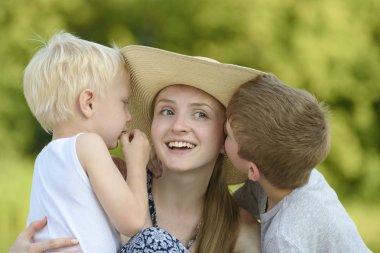 İki küçük oğlu anne sarılmak ve yeşillik zemin karşı yanaktan öpmek