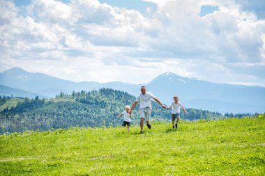 Baba ve yeşil orman, dağlar ve bulutlu gökyüzü arka plan üzerinde el ele tutuşarak yeşil alan çalışan iki genç oğlu.
