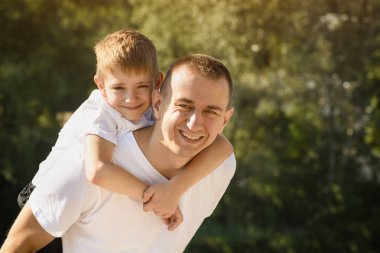 Arka açık havada küçük oğluyla mutlu baba. Uzakta bulanık yeşil ağaçlar. Dostluk ve babalık kavramı