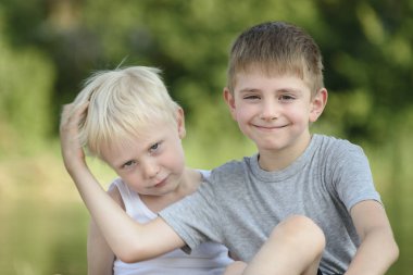 İki küçük çocuk dışarıda oturuyor. Uzakta bulanık yeşil ağaçlar. Dostluk ve kardeşlik kavramı
